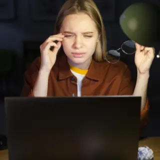 Kvinna som tagit av sig glasögonen och kämpar med att se vad som är på hennes datorskärm