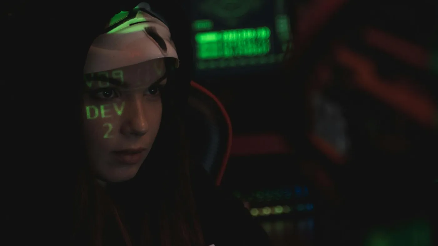 En kvinnlig spion i mörkt rum, med texten 'dev' projicerat i ansiktet